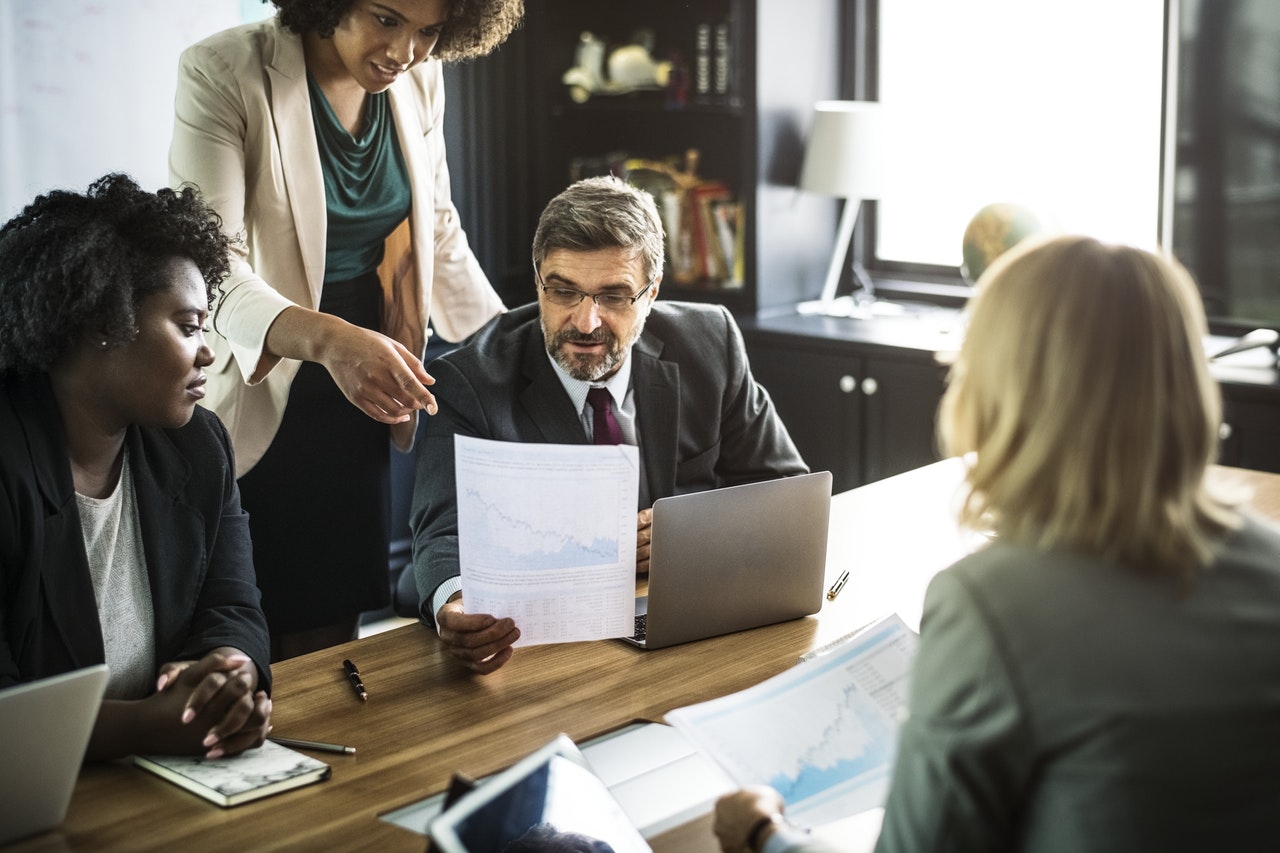 Professionals sat round a desk sharing information with one another on screen and via written documents